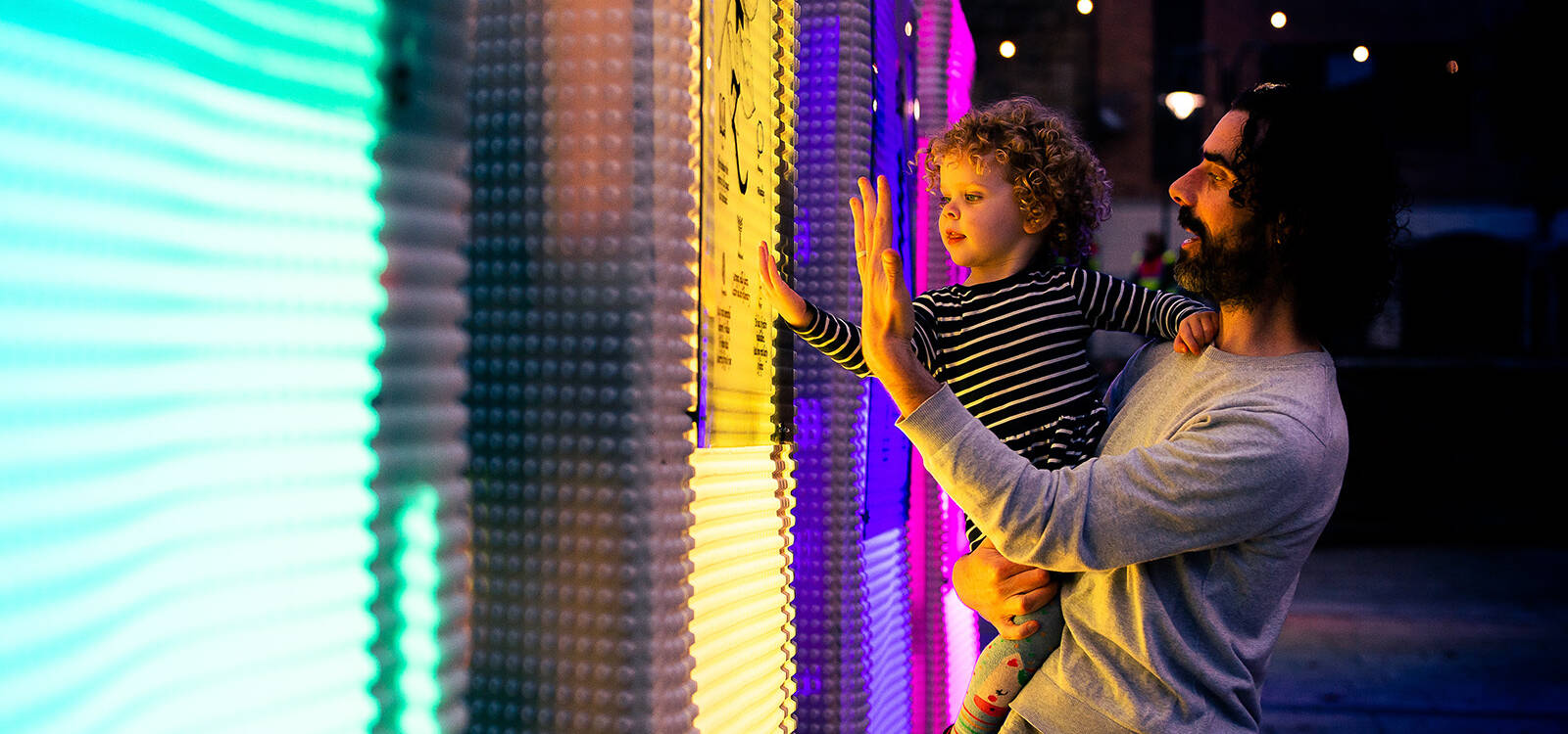 A parent holding their child looking at an art light installation