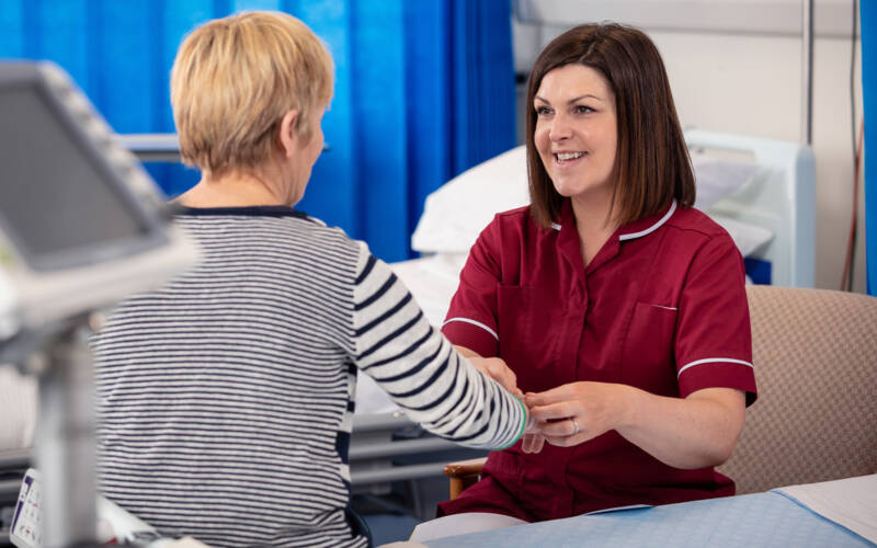 A nurse in a red uniform tends to a patient sitting on a hospital bed
