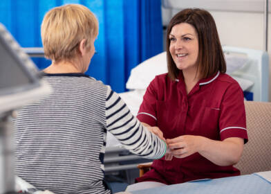 A nurse in a red uniform tends to a patient sitting on a hospital bed