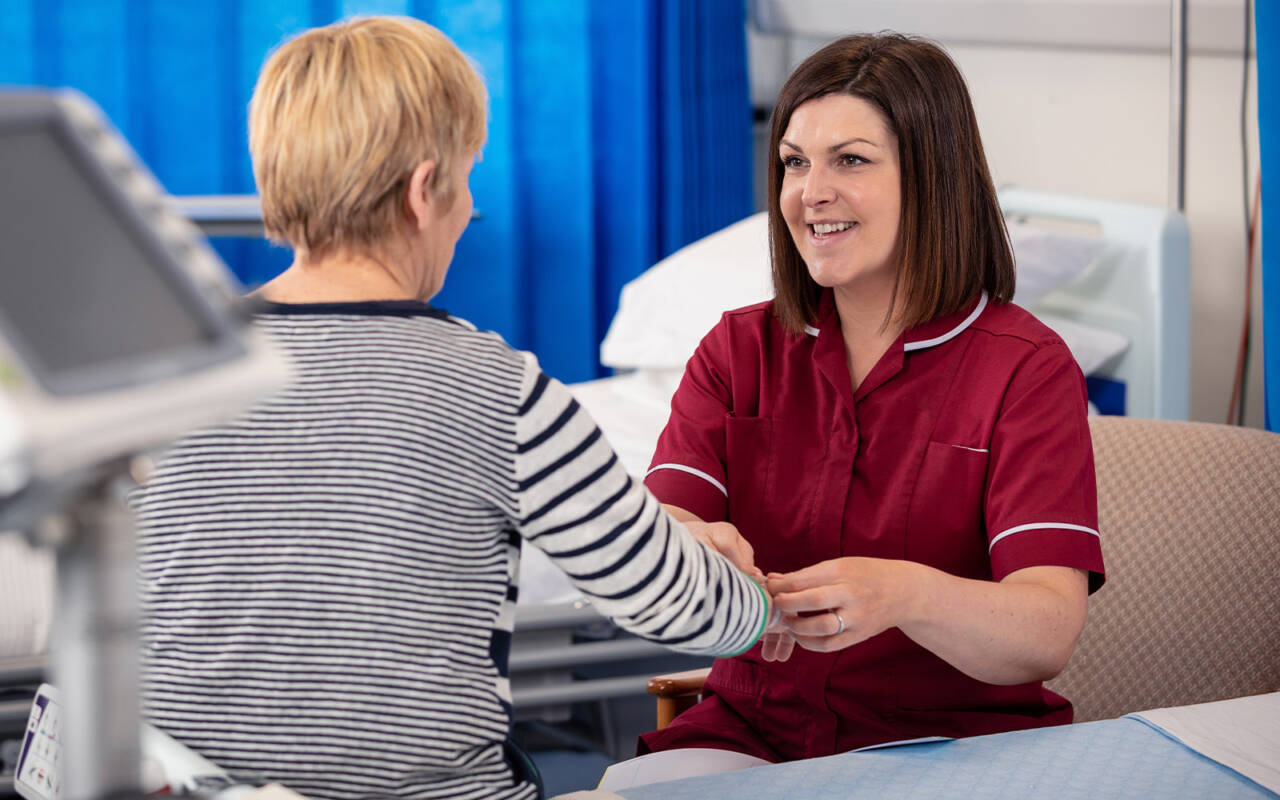 A nurse in a red uniform tends to a patient sitting on a hospital bed
